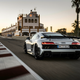 2023 audi r8 gt seen from the rear as it accelerates down the straightaway of a race track. there is a long building running parallel to the track in the background and the sun is setting